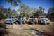 1989 Ford Bronco - Four lifted trucks and SUVs are parked in a dirt lot with people standing in front of them.
