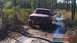1989 Ford Bronco - Red 1989 Ford Bronco navigating a wet, muddy path in a wooded area.