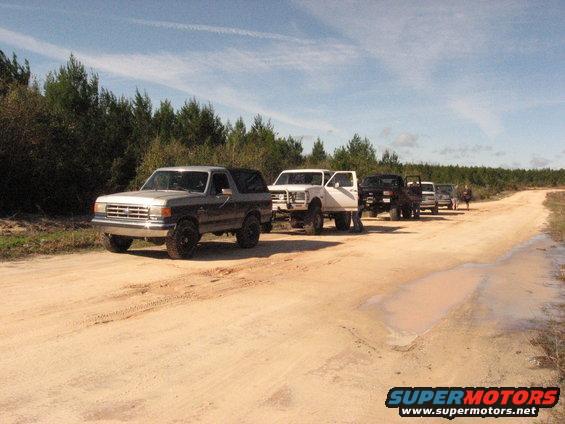 Silver 1987 Ford Bronco 3q-front view on dirt road with other vehicles
