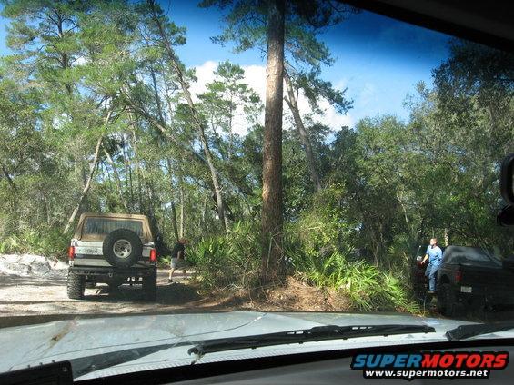 1989 Ford Bronco parked on dirt road, spare tire on rear door. Another vehicle is parked to the right