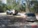 1989 Ford Bronco - Two SUVs navigate a sandy trail in a wooded area, one a lifted white 1989 Ford Bronco and the other a silver SUV.