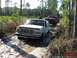 1989 Ford Bronco - Two trucks navigate a muddy path through a wooded area with tall trees and dry grass.