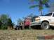 1989 Ford Bronco - Multiple Ford Broncos are lined up in a field under a clear blue sky.