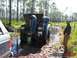 1989 Ford Bronco - Two men work on a 1989 Ford Bronco stuck in a muddy, wooded area while another watches.