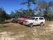 1989 Ford Bronco - A line of four SUVs, including a white 1992 Ford Bronco, are parked outdoors on a sunny day.