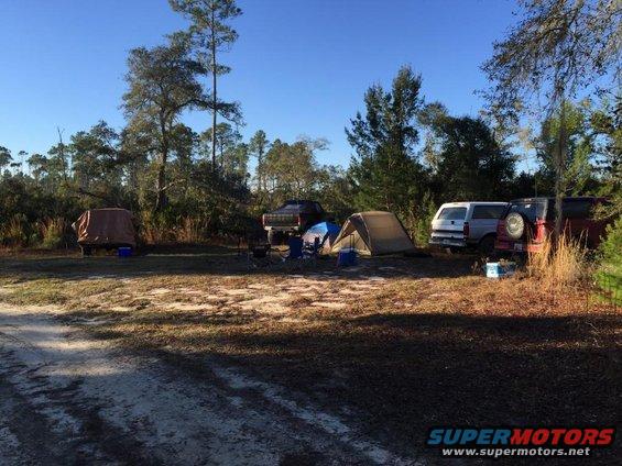 Campsite scene with a red Ford Bronco, a white SUV, and a brown pickup truck parked near tents