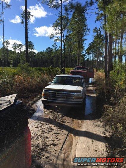 White Ford F-150 truck driving through mud, front view. Grille indicates 1992 model year
