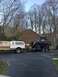 1989 Ford Bronco - A brown and white pickup truck tows a black lifted truck on a trailer in a driveway.