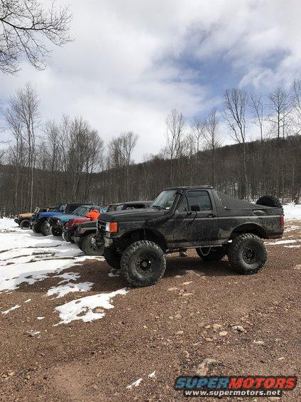 Black lifted Ford Bronco with large tires parked on a dirt road with snow patches