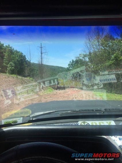 View from inside a vehicle looking out at a dirt road with trees and a power line tower