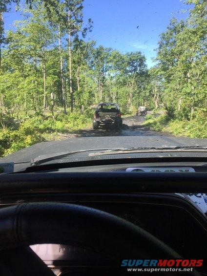 Black Ford Bronco driving on a muddy trail, viewed from inside another vehicle