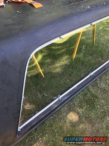 Close-up of a black vehicle hard top with a window frame and reflection of yellow supports