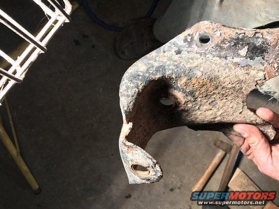 Hand holding a heavily rusted metal bracket with holes, possibly a suspension component