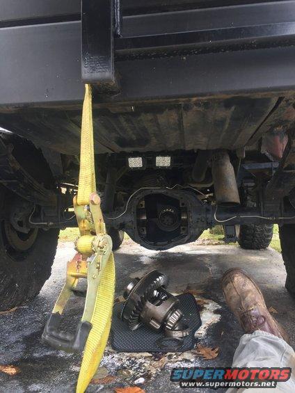 Differential removed from a vehicle's rear axle, with a yellow ratchet strap attached to the frame