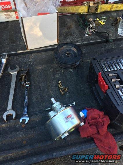 Power steering pump with part number SN1-11699, pulley, wrenches, and socket set on a truck bed