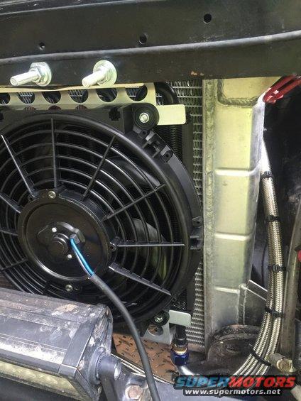 Close-up of an aftermarket radiator fan mounted in front of a cooling system. Includes braided hoses and a light bar