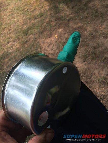 Close-up of a shiny metal gauge with a green hose fitting attached. A hand is holding it