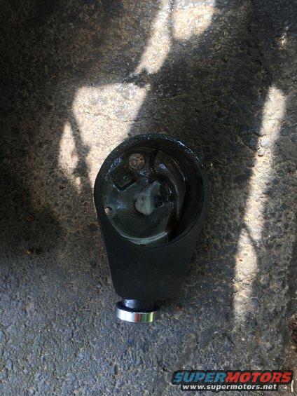 Black steering column component with silver trim ring, resting on asphalt