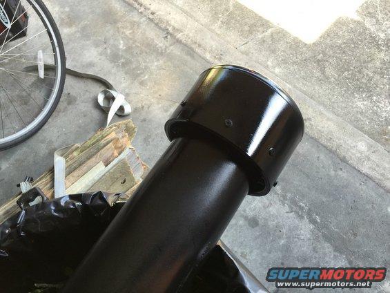 black snorkel pipe with screws, next to wood scraps and a bicycle wheel