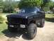 1989 Ford Bronco - This modified pickup truck has large off-road tires and a matte black finish. Another vehicle is visible in the background.