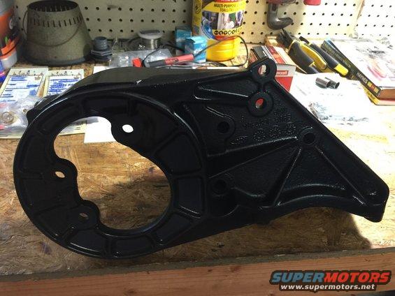 Black metal engine bracket with circular opening and mounting holes on a wooden surface