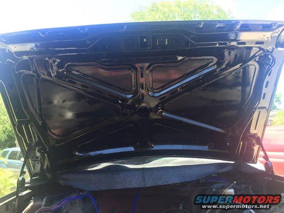 underside of black car hood, some engine parts visible below