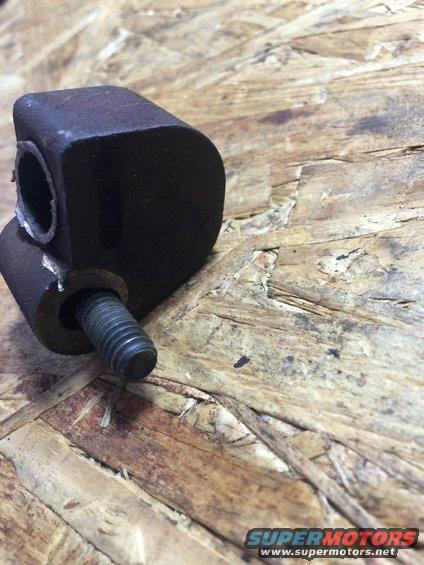Rusty metal engine mount bracket with a threaded bolt protruding from one side, resting on a wooden surface