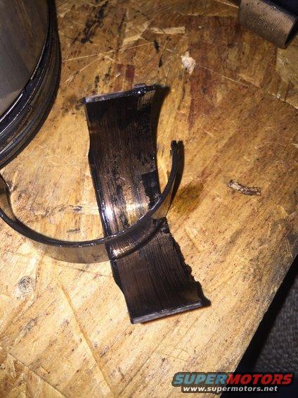 Broken engine bearing with black residue on a wooden surface