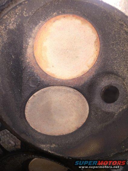Engine cylinder head with two valves, one larger than the other, showing carbon buildup