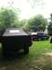 1989 Ford Bronco - Rear view of a black pickup truck with a soft top, with a dark SUV in the yard.
