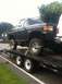 1989 Ford Bronco - A lifted Ford Bronco is secured with straps on a flatbed trailer, ready for transport.