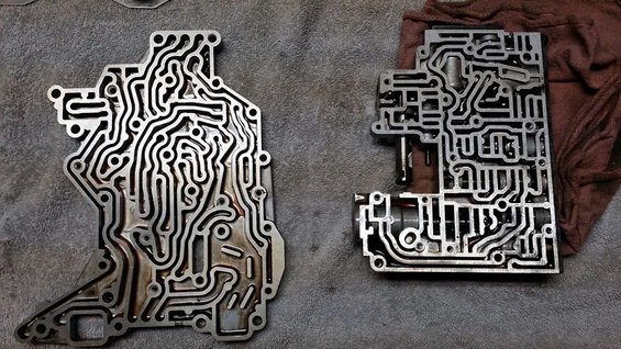 Two metal transmission valve bodies with complex channels on a gray surface