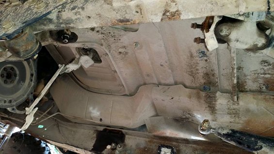 Underside view of a vehicle showing the transmission bell housing, exhaust pipe, and fuel tank