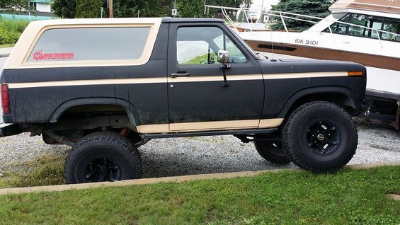 Black Ford Bronco with tan top and stripe, parked next to a boat