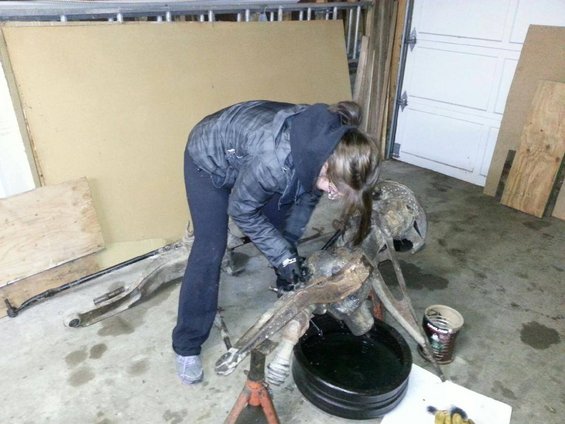 Vehicle suspension parts on a jack stand with a person working on them in a garage