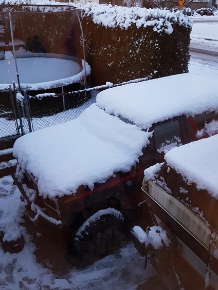 Brown SUV covered in snow, parked next to another vehicle. Visible tire and part of the door