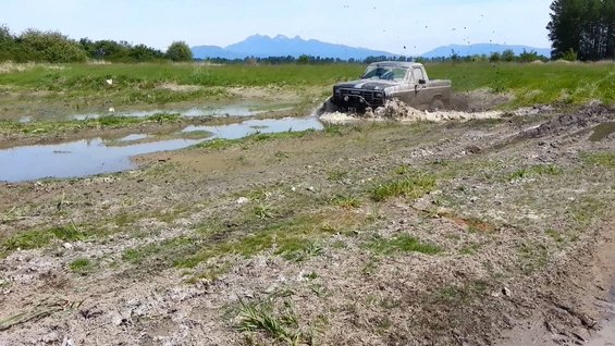 Pickup truck driving through mud and water, kicking up spray. Mountains in background