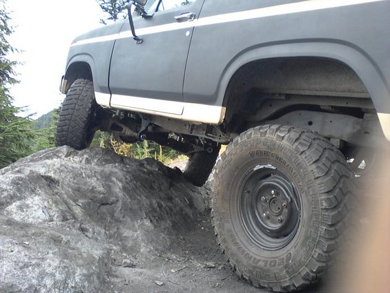 Modified Ford Bronco with large tires climbing over rocks