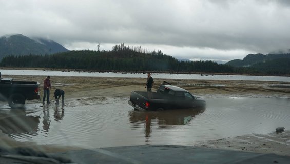 Black pickup truck partially submerged in muddy water with two people nearby