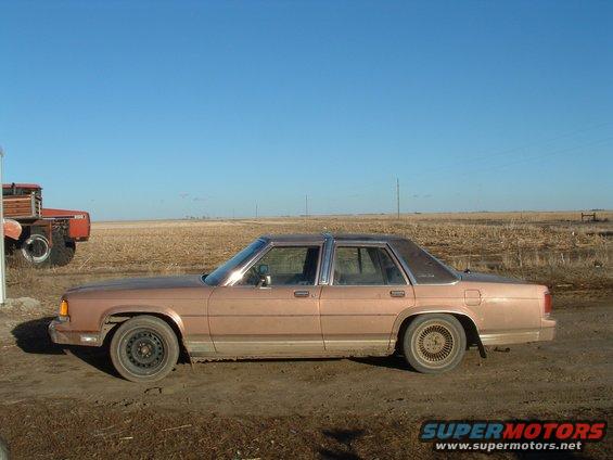 tan sedan parked in a dirt lot with a red tractor in the background