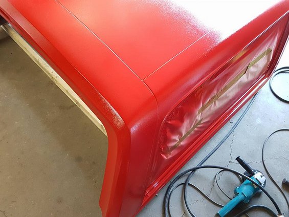 Red painted vehicle body panel with masking tape over a window opening, angle grinder nearby