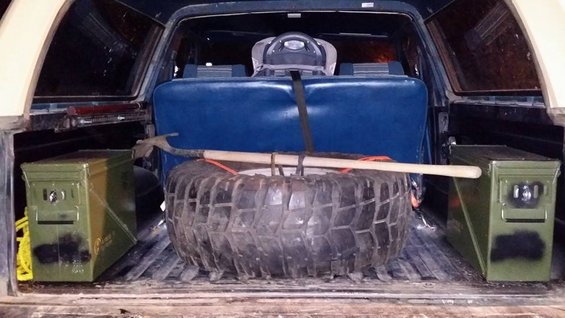 Spare tire, shovel, and two green ammo cans secured in the cargo area of an older SUV