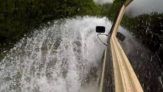 Side view of a vehicle splashing through water on a wooded road