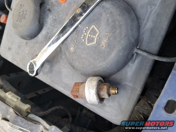 Engine bay with a sensor removed and a wrench on top of a fluid reservoir