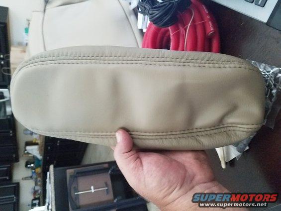Tan leather armrest with double stitching held by a hand. Background shows car interior parts and wiring