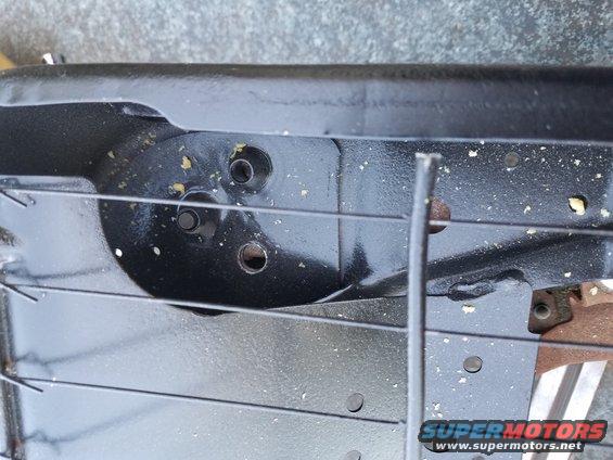 Black metal seat frame with visible mounting holes and some debris. A Supermotors.net logo is in the lower right corner