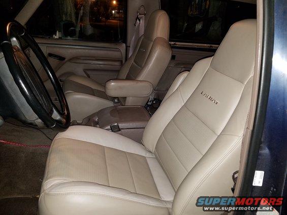 Front seats of a truck, tan leather with two-tone inserts. Armrest console between seats. Steering wheel visible