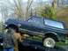 1989 Ford Bronco - A dark green Ford Bronco is being loaded onto a tow truck, with two individuals attending to it.