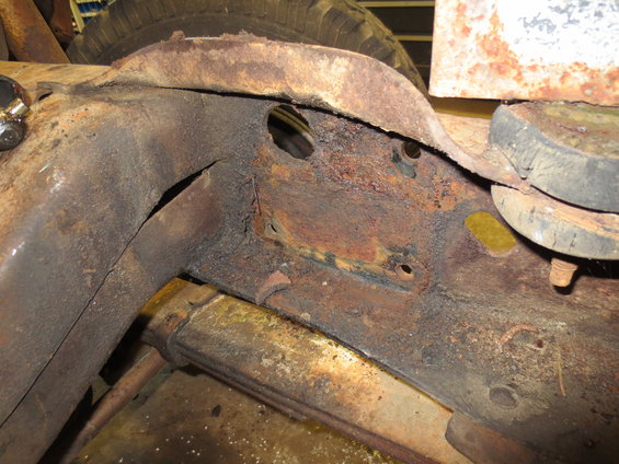 Close-up of heavily rusted truck frame with visible leaf spring and tire in background