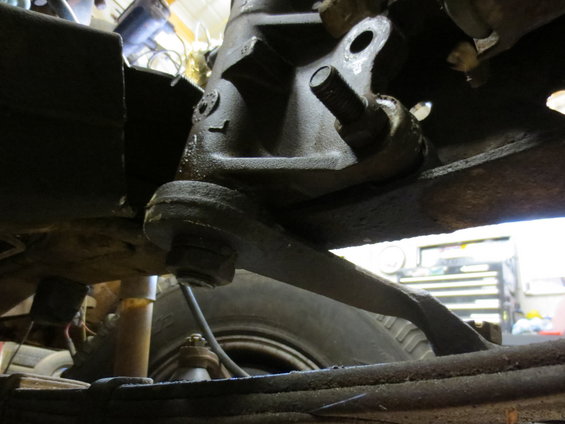 Close-up of a truck's steering knuckle and tie rod end, with a tire and leaf spring visible below